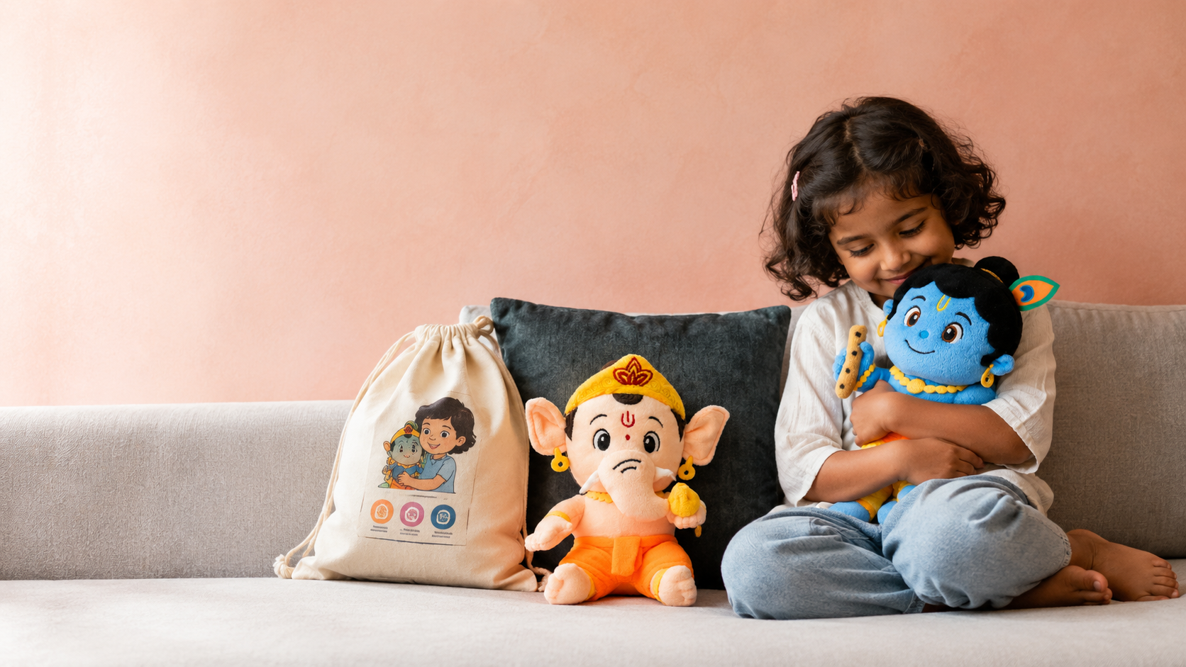 A grandmother and her granddaughter sitting together, the child holding a Clapstore mantra-chanting Ganesha plush while her grandmother guides her finger to the belly button